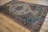 Vintage Persian Baktiari rug viewed from an angle, showing its ivory floral field and dark indigo spandrels.
