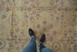 Feet on dusty gold Khotan rug, highlighting abrash and pale red pomegranate motifs.