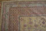 Hand-knotted Khotan rug corner, dusty gold field with pale red and mauve pomegranate motifs.