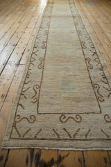 Long distressed Khotan runner with a subtle abrashed beige field and scrolling brown border.