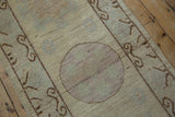 Distressed Khotan rug with mauve roundel medallion and brown scrolling ram's horn border.