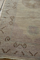 Distressed beige Pakistani Khotan design rug with mauve scrolling patterns and aged texture.