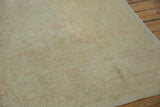 Textured detail of distressed Oushak rug, soft beige, ivory, and faint blush floral patterns.