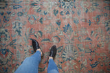 Feet on distressed Mahal carpet, highlighting worn pile, faint foundation, muted rose, teal.