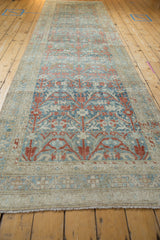 A long view of a distressed Persian Hamadan runner showing its repeating blue and terracotta vinery pattern.