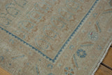 Distressed Hamadan rug corner displaying beige boteh motifs, blue serrated border, and fringe.