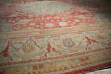 Oushak rug detail: ivory spandrel, wide border, cinnabar red field, floral arabesques, even wear.