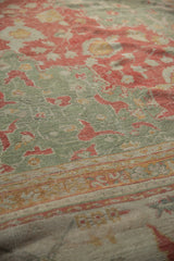 Traditional Oushak rug's cinnabar red vinery and seafoam green pile, showing wear and border detail.