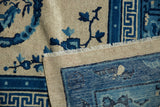 Folded close-up of antique Chinese Ningxia carpet, hand-knotted pile, blue lotus motif, beige field, fringe.