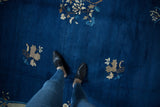Cobalt blue field of the Vintage Peking carpet with beige floral sprays, showing a person.