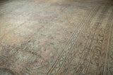 Oushak rug, thick pile showing distressed meandering vine borders and soft floral patterns.