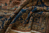 Folded vintage Mahal rug; ornate terracotta, navy, gold floral vinery and white fringe.