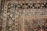 Distressed vintage Mahal carpet corner, showing faded brick red, black, and beige floral vinery.
