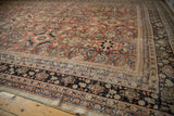 Distressed vintage Mahal carpet corner with brick red field, exposed foundation, and worn black border.