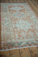 The linear pattern of a distressed Karaja rug viewed from an angle in soft blush and seafoam tones.