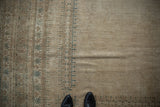 Distressed vintage Afghan carpet's worn pile, pale coffee field, and geometric slate blue border.