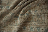 Textured vintage Afghan carpet showing distressed geometric motifs in muted beige and slate blue.