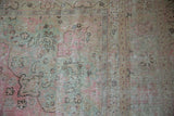 Distressed Meshed carpet with faded bubblegum pink, seafoam green, and beige floral motifs.
