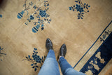 Feet on hand-knotted vintage Peking rug, showcasing beige field and blue floral vase motif.