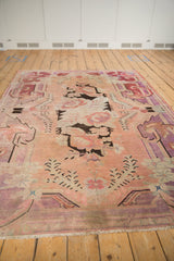 Distressed Khotan carpet showing pale violet, blush, and dark curvilinear floral patterns and fringe.