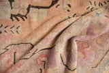 Distressed Khotan carpet pile showing softened blush, violet, and dark brown curvilinear patterns.