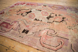 Distressed vintage Khotan carpet showing faded blush, violet, and brown floral designs.