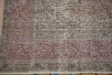 Close-up on the distressed, low-pile texture of a vintage Tabriz carpet's floral border.