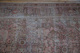 Distressed vintage Persian rug with faded pink, mauve, gray floral patterns showing knot head wear.