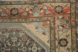 Corner detail of a distressed Borchalou rug showing its floral vine border and worn pile.