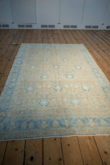 Angled view of a distressed Persian Hamadan rug with a decorative sand and powder blue pattern.