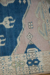 Distressed Oushak rug close-up: short pile in dusty cobalt blue, pale mauve, and ivory motifs.