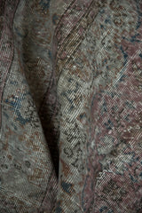 Distressed texture and folded pile of vintage Sparta rug, dusty raspberry and charcoal.
