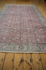 Close-up of distressed Sparta carpet's worn red floral pattern, muted green border, and fringe.