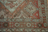 Intricate geometric border of a distressed Soumac carpet with hook-and-latch motifs in chestnut and slate blue.
