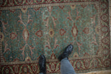 Distressed vintage Kayseri rug featuring an ocean green field, red floral border, and heavy abrashes.