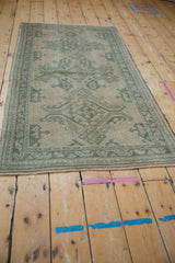 Distressed vintage Oushak runner's celadon green floral vines, beige field, and even pile wear.