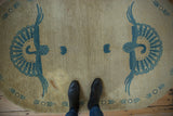 Overhead view of vintage oval Art Deco rug with double blue peacock design on beige, showing stain.