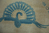Elegant blue peacock motif with fanned tail detail on a beige Art Deco Chinese rug.