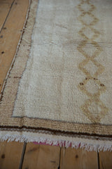 Fringed end of a vintage Moroccan rug, highlighting intact selvage and beige diamond motif.