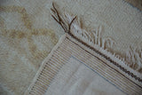 Thick cream pile, dark brown fringe, and striped woven foundation of a vintage Moroccan rug.