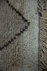 Vintage Moroccan rug pile with primitive dark brown geometric motifs, natural ivory, and braided fringe.