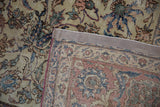 Distressed vintage Isfahan carpet showing worn ivory and blue vinery, with edge folded to reveal foundation.