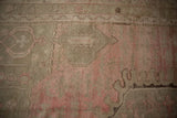 Geometric floral arabesques in light rose and beige on a distressed hand-knotted pile.