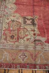 Worn, low pile of a vintage Oushak carpet corner with sand and dusty red patterns.