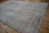 Angled view of a vintage Bijar's faded pink floral border and time-softened low pile.
