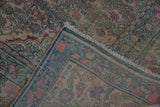 Corner of the vintage distressed rug showing its hand-knotted back and intact side cord.