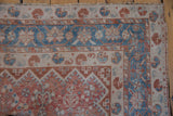 Ornate geometric borders in faded red and sky blue on a distressed vintage Qashqai rug corner.