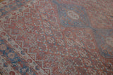 Angled view of a distressed Qashqai carpet's low pile and faded geometric field.