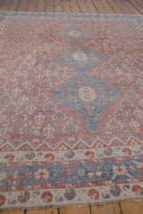 Angled view of the ornate lattice field and blue medallions on a distressed vintage Qashqai carpet.