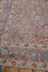 Detail of the ornate borders and worn field of a vintage Qashqai rug in faded reds and blues.